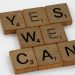 Wooden Scrabble tiles arranged to spell 'Yes We Can', emphasizing motivation on a white backdrop.